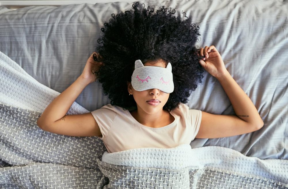 Woman with eye mask lying on her back in bed