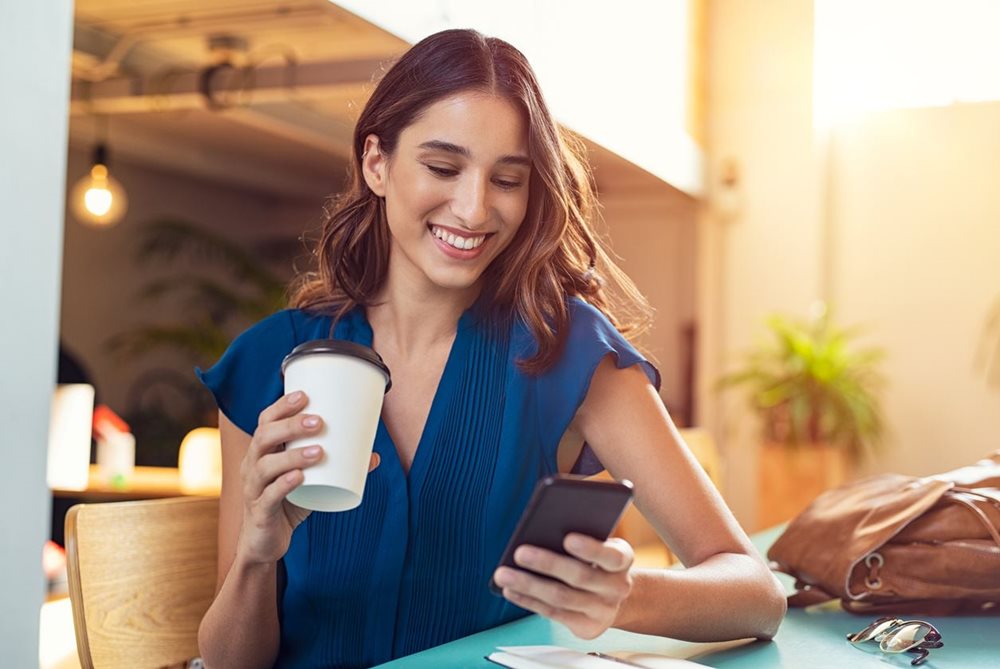 Woman looking at mobile drinking coffee